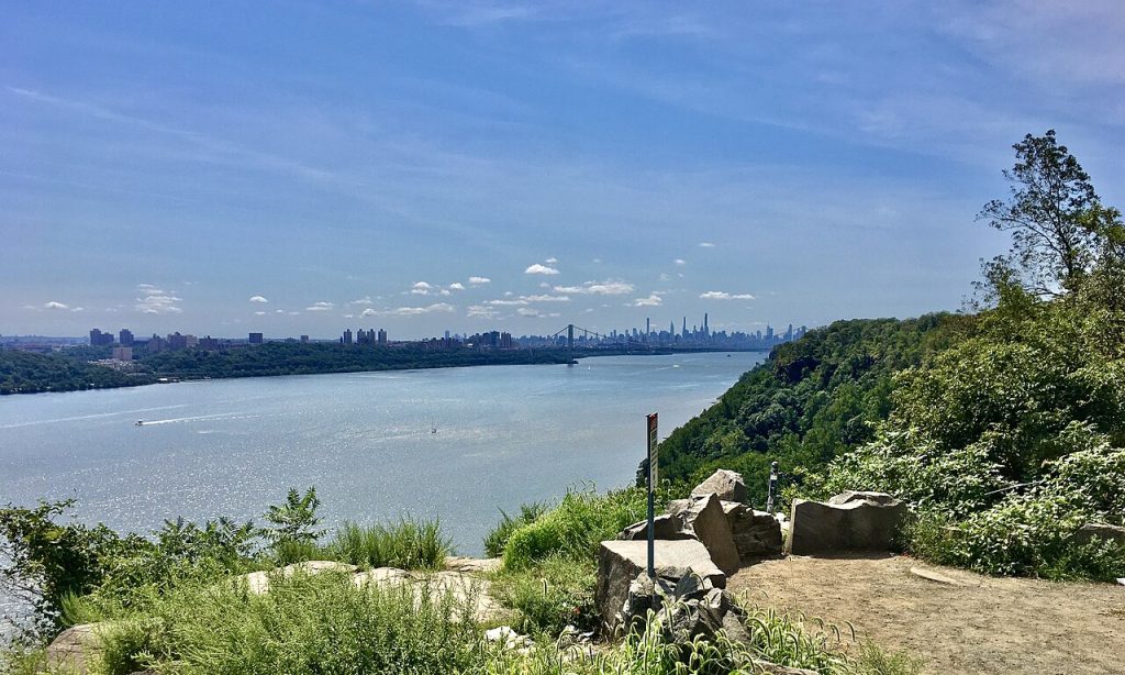 Scenic view of the Hudson River and skyline of New York City from Palisades Interstate Parkway in Englewood Cliffs, NJ, highlighting the area's natural beauty and elevated terrain.