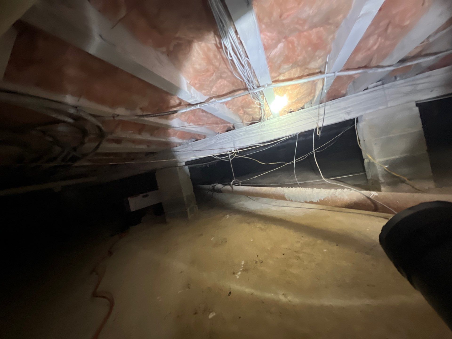 Damp crawl space under a New Jersey home showing exposed insulation and moisture before encapsulation.
