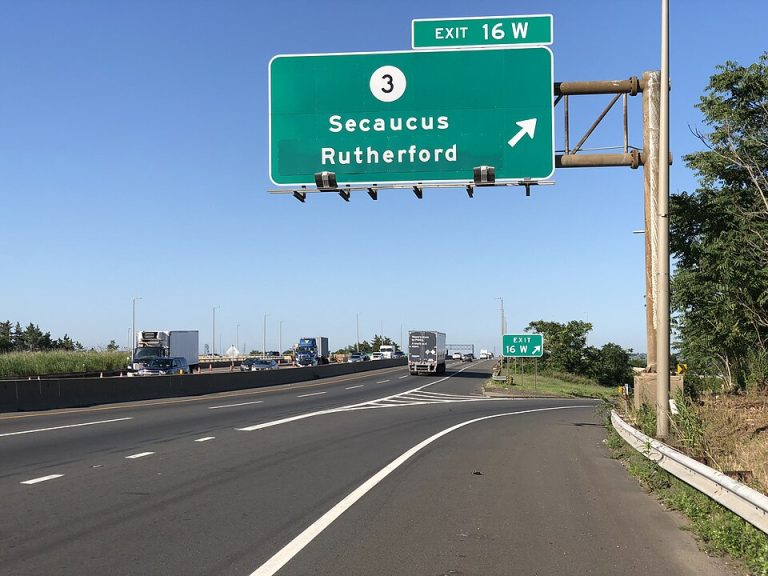 Highway exit sign for Secaucus and Rutherford, indicating Exit 16W, with clear blue sky and vehicles on the road, relevant for local waterproofing and mold remediation services in East Rutherford, NJ.