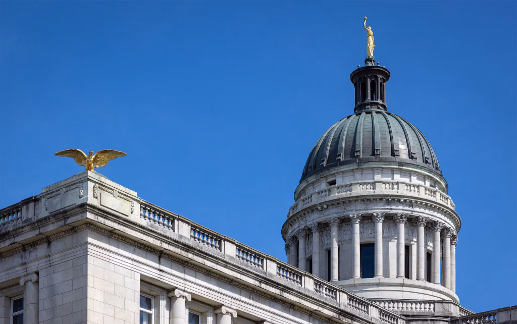 Gold eagle statue atop a building, with a dome featuring a statue of a woman, against a clear blue sky, symbolizing governance and architecture in Hackensack, NJ.