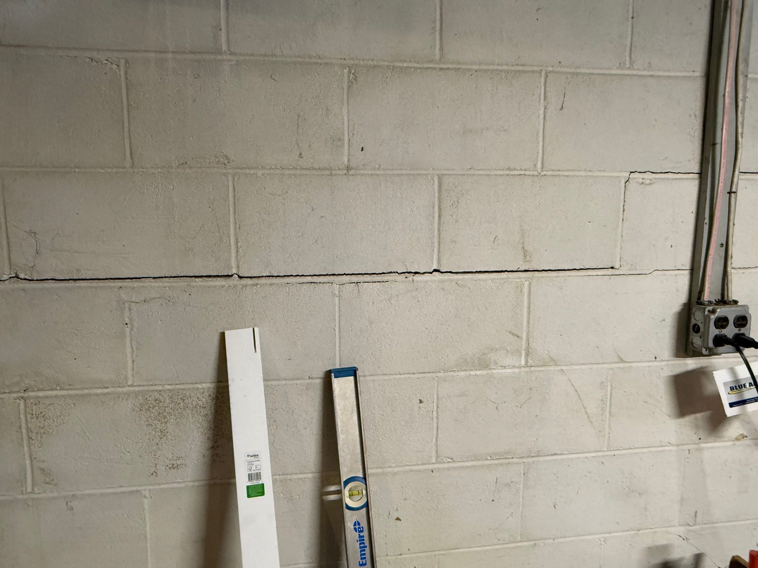 Foundation crack repair in New Jersey basement wall with measuring tool.