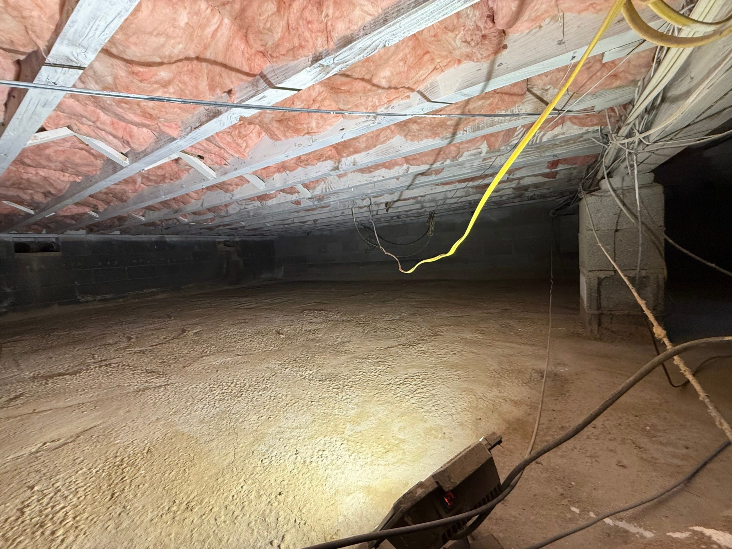 Unencapsulated crawl space in a New Jersey home with exposed soil, fiberglass insulation between floor joists, and concrete block foundation walls.